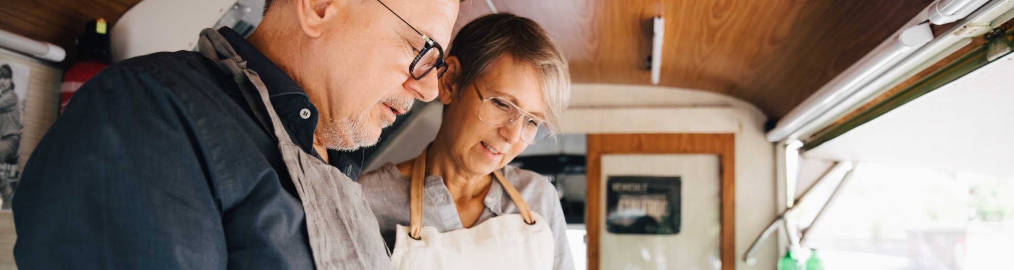Mature owners looking at order while standing in food truck 
